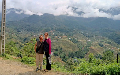 Tourists on a Sapa motorbike tour with terraced rice fields and mountains in the background.