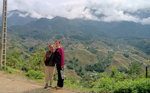Tourists on a Sapa motorbike tour with terraced rice fields and mountains in the background.