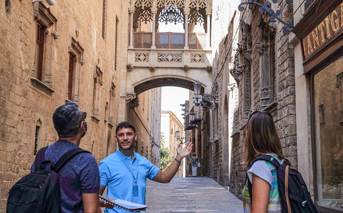 Tour guide leading visitors through Barcelona's Gothic Quarter under the Bishop's Bridge.