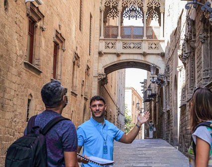 Tour guide leading a group through Barcelona's Gothic Quarter under the Bishop's Bridge.