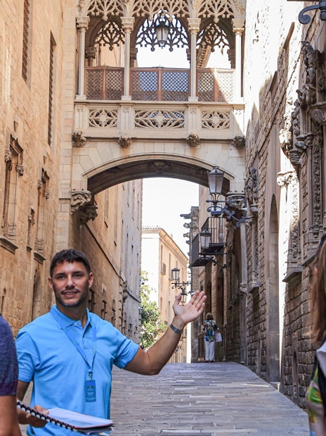 Tour guide leading a group through Barcelona's Gothic Quarter under the Bishop's Bridge.