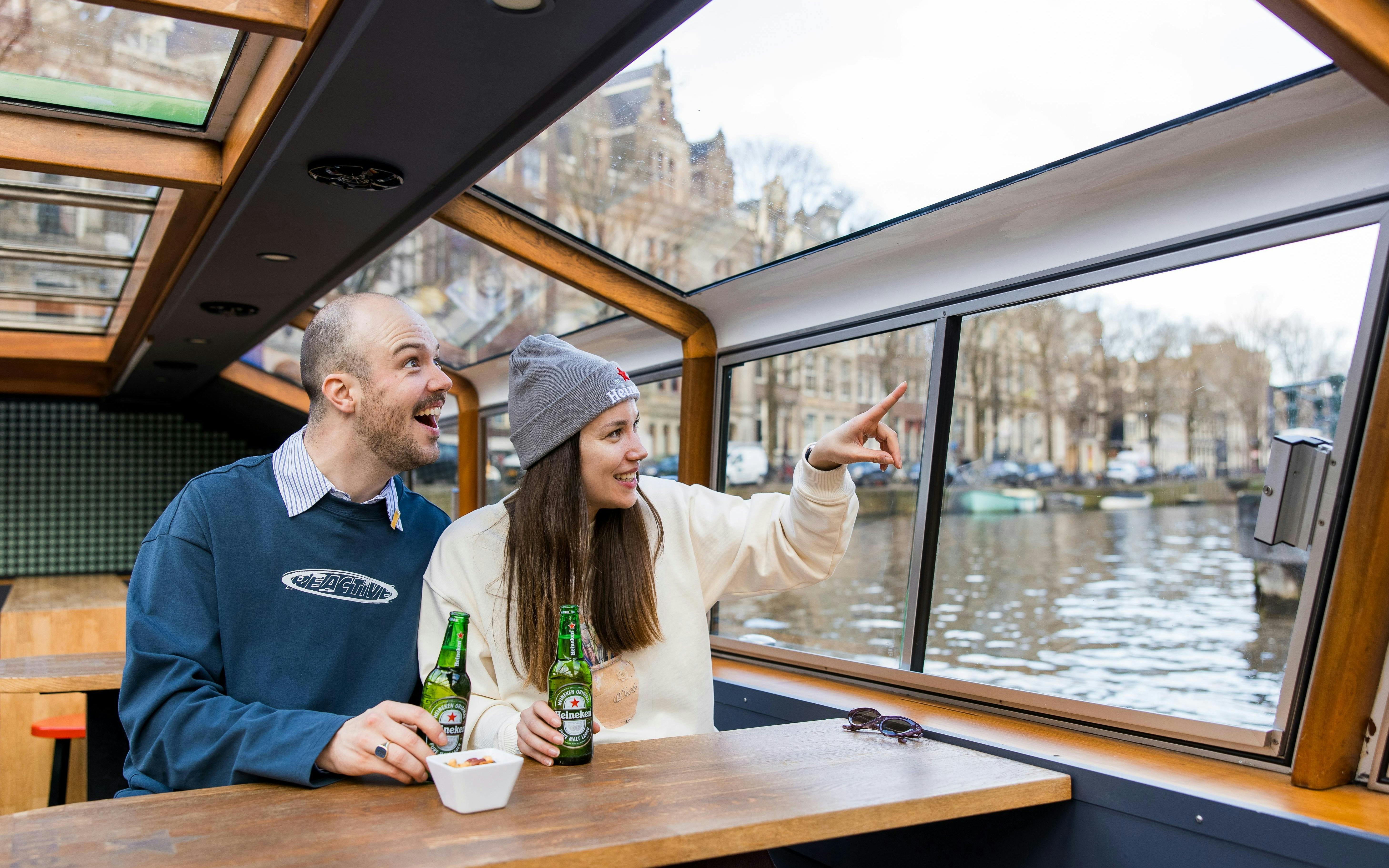 Couple enjoying Heineken cruise with drinks on Amsterdam canal boat.