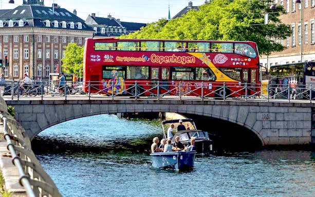 Copenhagen hop-on hop-off bus on bridge with canal cruise below.