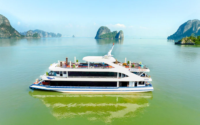 Harmony cruise ship sailing in Ha Long Bay with limestone islands in the background.