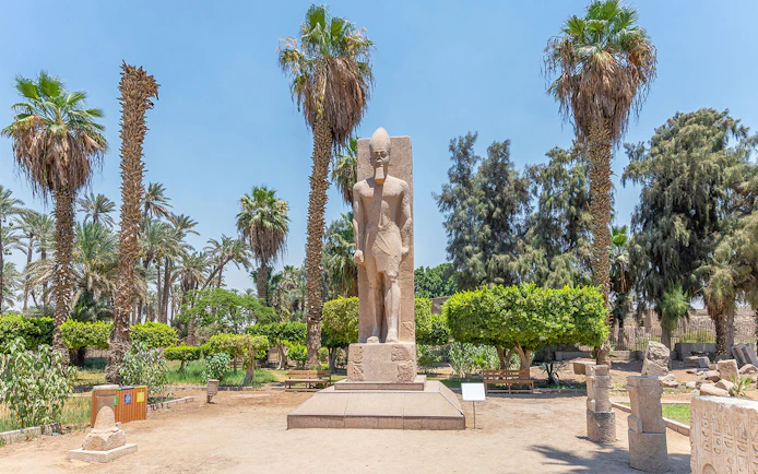 Statue of Ramses II surrounded by palm trees in Memphis, Egypt.