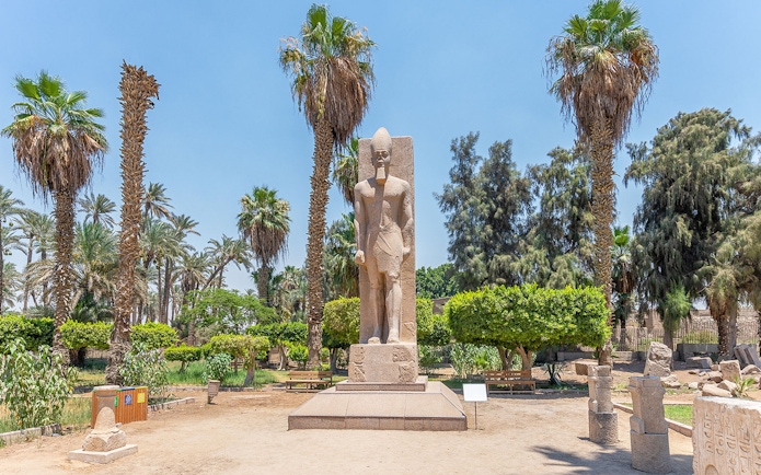 Statue of Ramses II surrounded by palm trees in Memphis, Egypt.