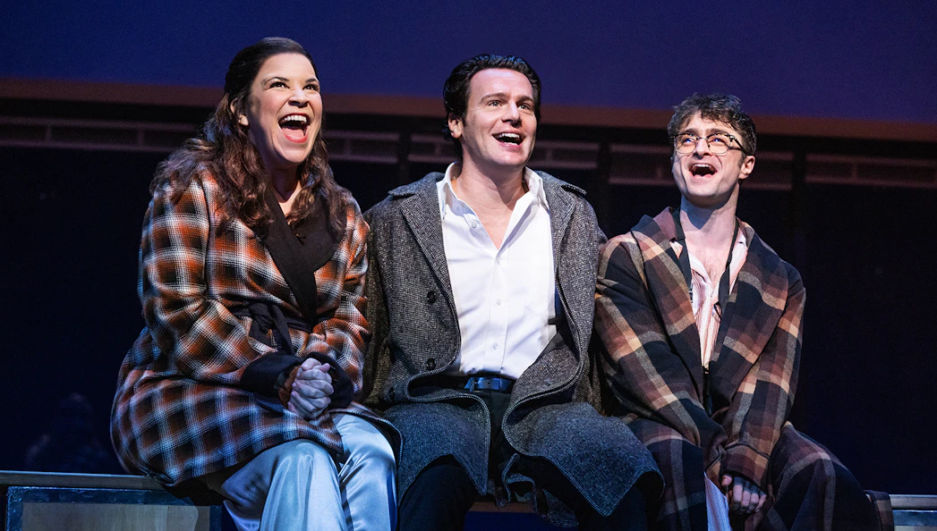 Three actors on stage performing in "Merrily We Roll Along" musical.