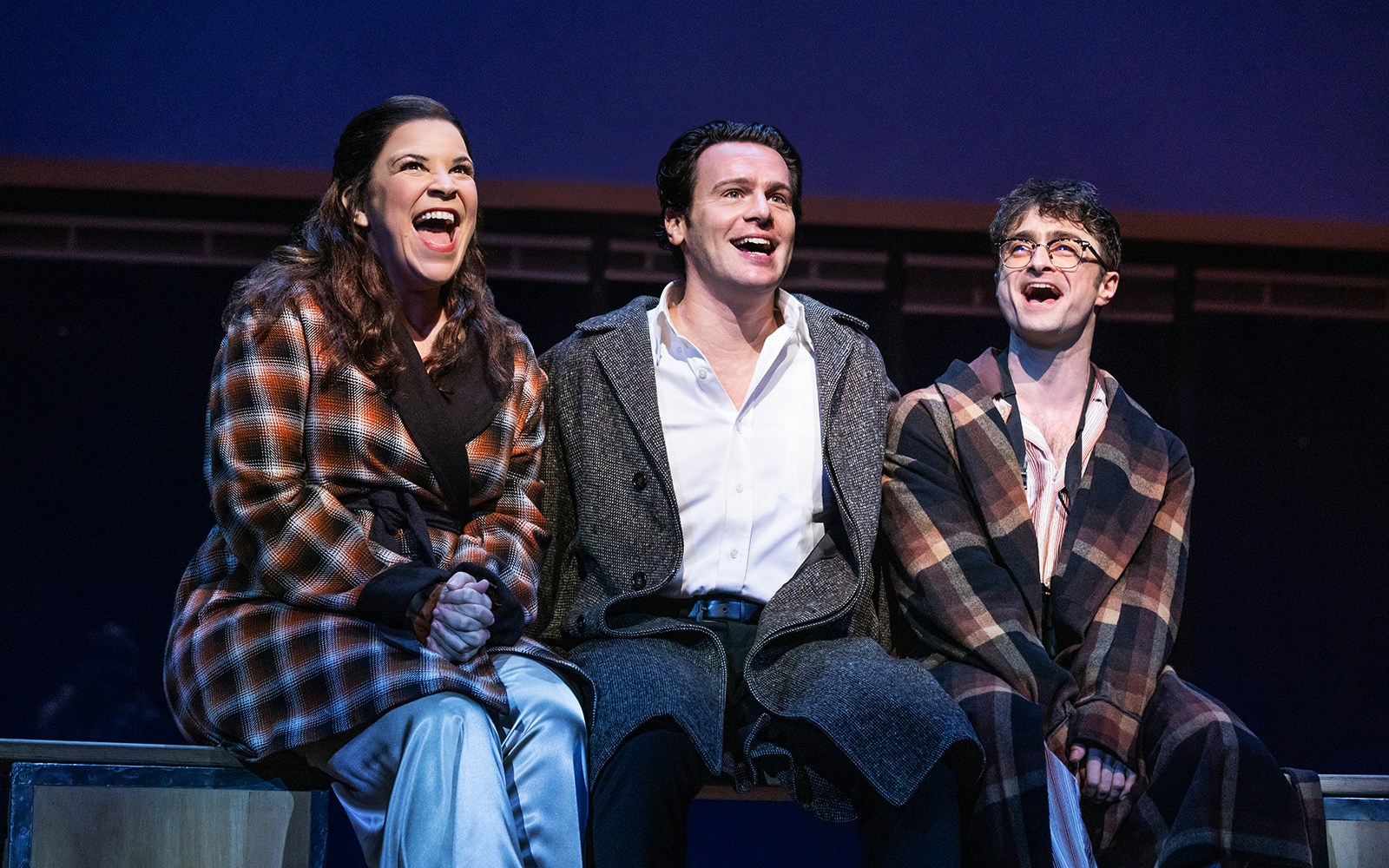 Three actors on stage performing in "Merrily We Roll Along" musical.