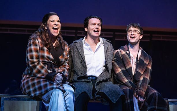 Three actors on stage performing in "Merrily We Roll Along" musical.