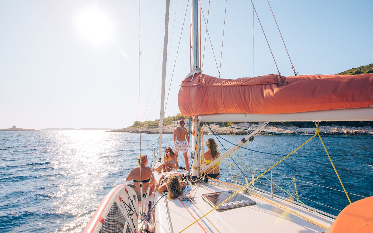 Yacht sailing near Hvar with people relaxing on deck under the sun.