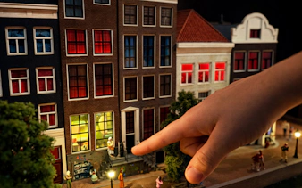 Miniature Amsterdam street scene with hand pointing at detailed buildings.