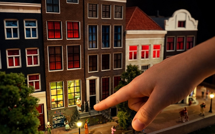 Miniature Amsterdam street scene with hand pointing at detailed buildings.