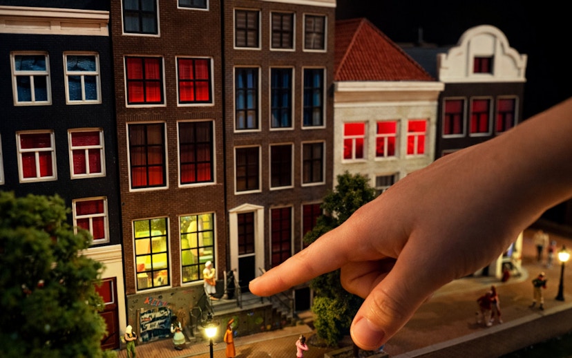 Miniature Amsterdam street scene with hand pointing at detailed buildings.