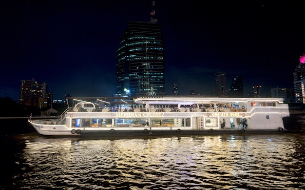 Meridian Cruise boat on Chao Phraya River at night, Bangkok skyline in background.