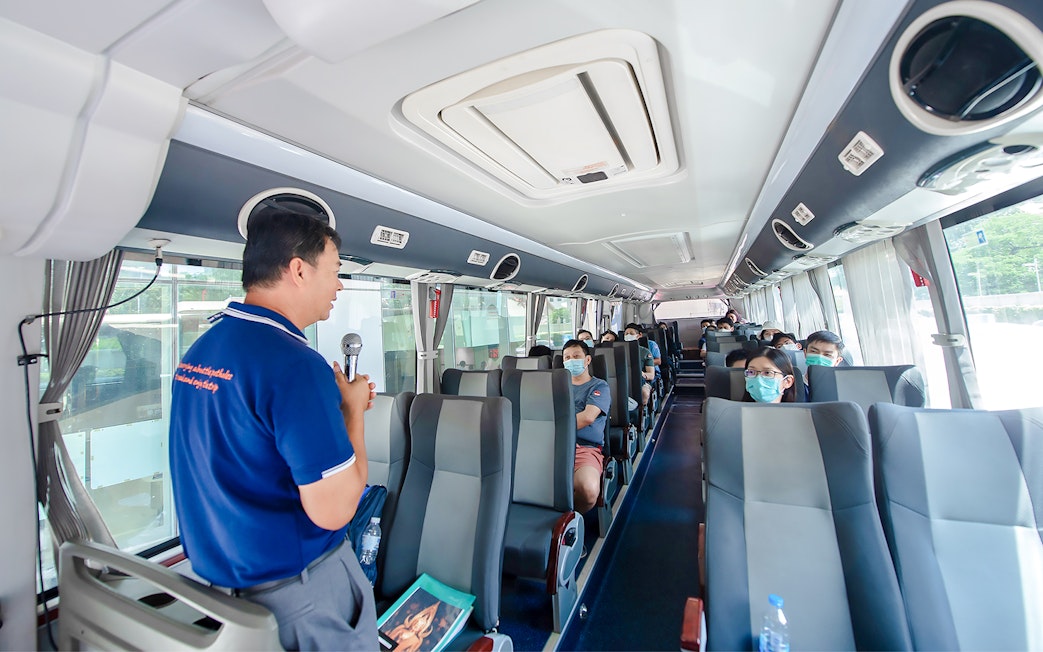Tour guide explaining Amphawa's history to tourists on a bus in Thailand.