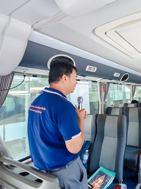 Tour guide explaining Amphawa's history to tourists on a bus in Thailand.
