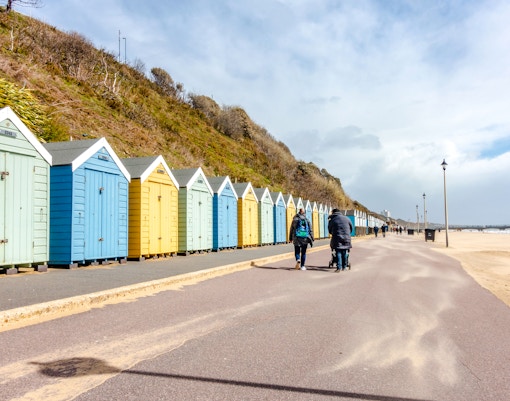People walking along beach huts at Bournemouth Beach on a sunny day.
