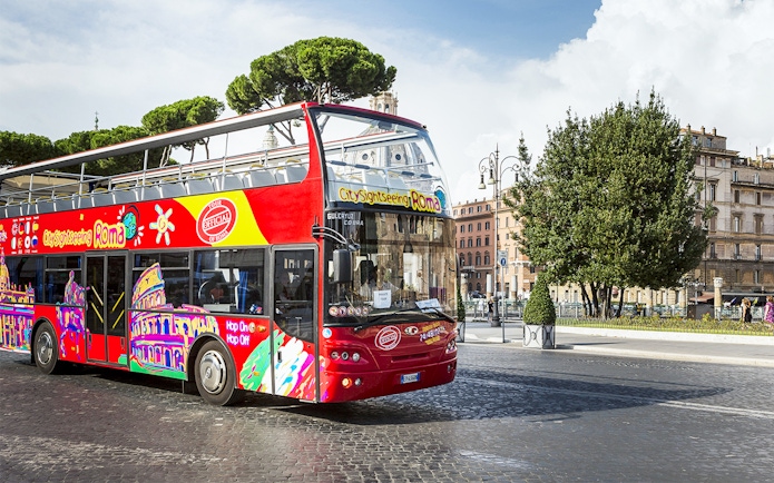Open-top sightseeing bus in Rome near historical buildings.