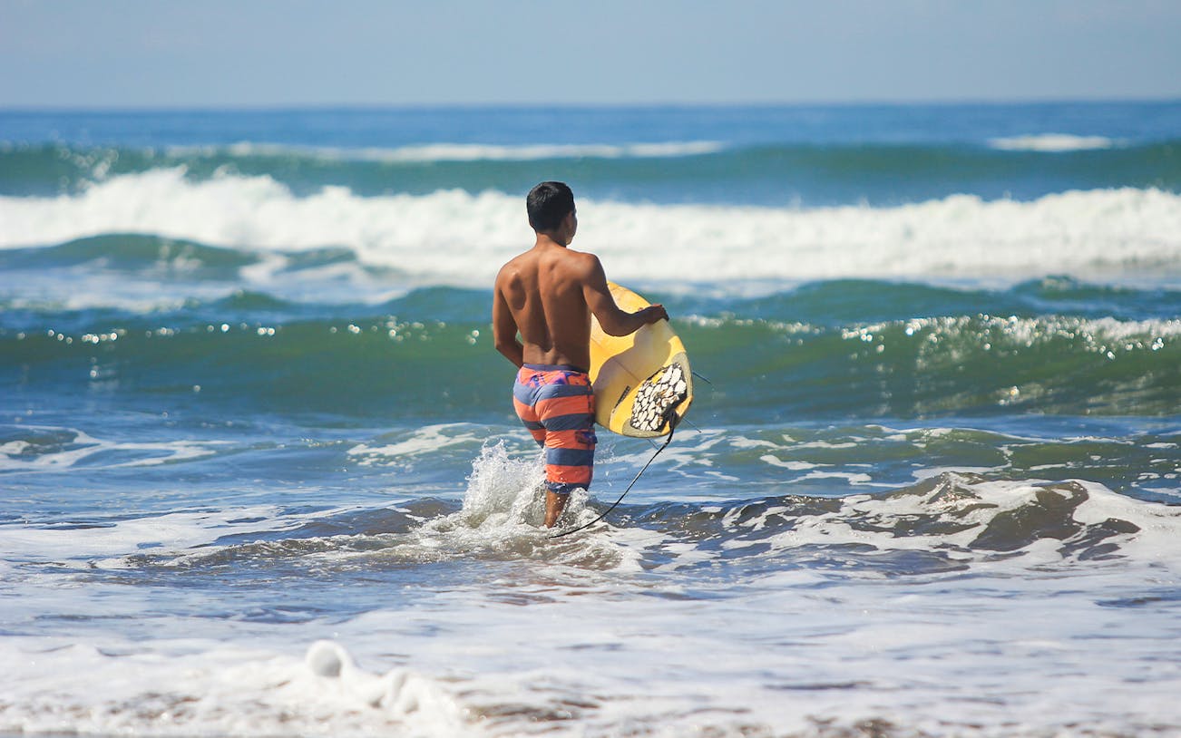 Surfer entering ocean waves, West Java coast, part of 3-day tour from Yogyakarta.