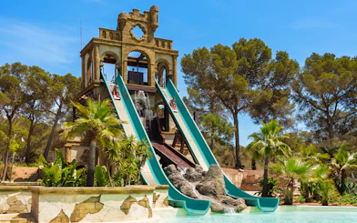 Banzai ride water slides at Aqualand El Arenal with lush greenery and clear sky.
