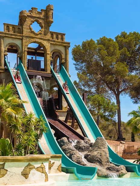 Banzai ride water slides at Aqualand El Arenal with lush greenery and clear sky.