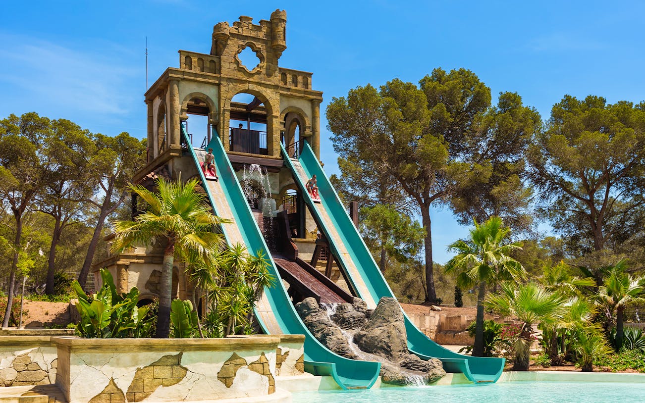 Banzai ride water slides at Aqualand El Arenal with lush greenery and clear sky.