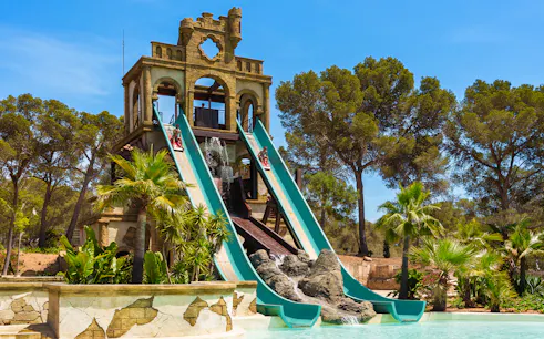 Banzai ride water slides at Aqualand El Arenal with lush greenery and clear sky.