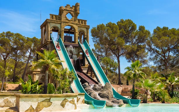 Banzai ride water slides at Aqualand El Arenal with lush greenery and clear sky.