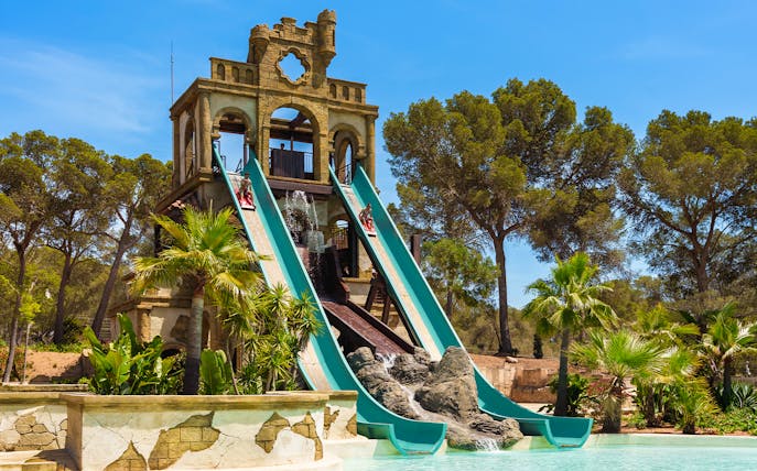 Banzai ride water slides at Aqualand El Arenal with lush greenery and clear sky.