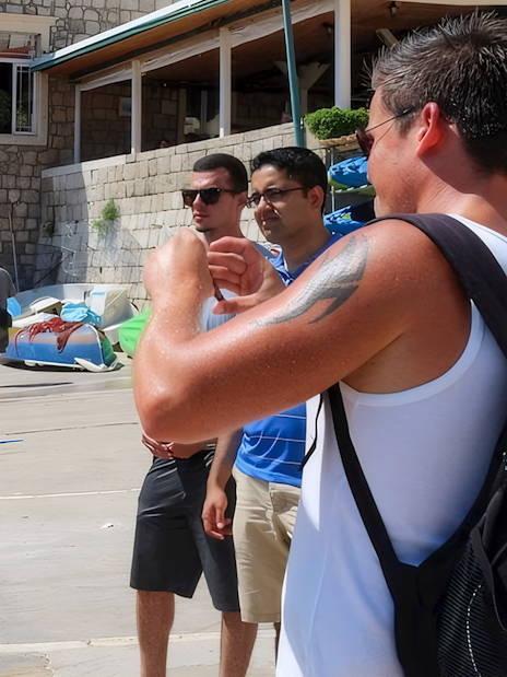 Female guide showing Game of Thrones location to tourists near kayaks and stone building.