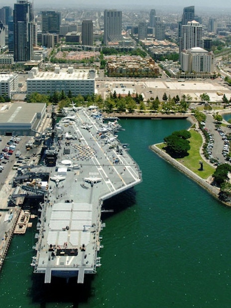 USS Midway Museum aircraft carrier docked in San Diego harbor with city skyline.