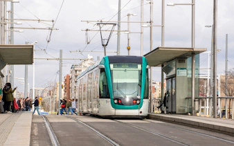 Tram at a Barcelona station with passengers boarding, part of the Hola Barcelona tour.