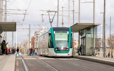 Tram at a Barcelona station with passengers boarding, part of the Hola Barcelona tour.