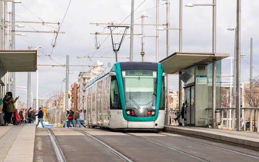 Tram at a Barcelona station with passengers boarding, part of the Hola Barcelona tour.