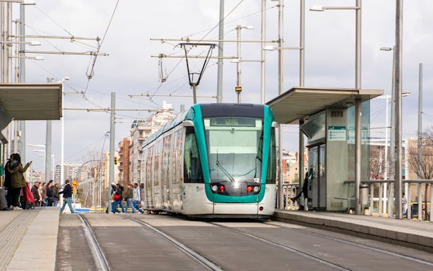 Tram at a Barcelona station with passengers boarding, part of the Hola Barcelona tour.