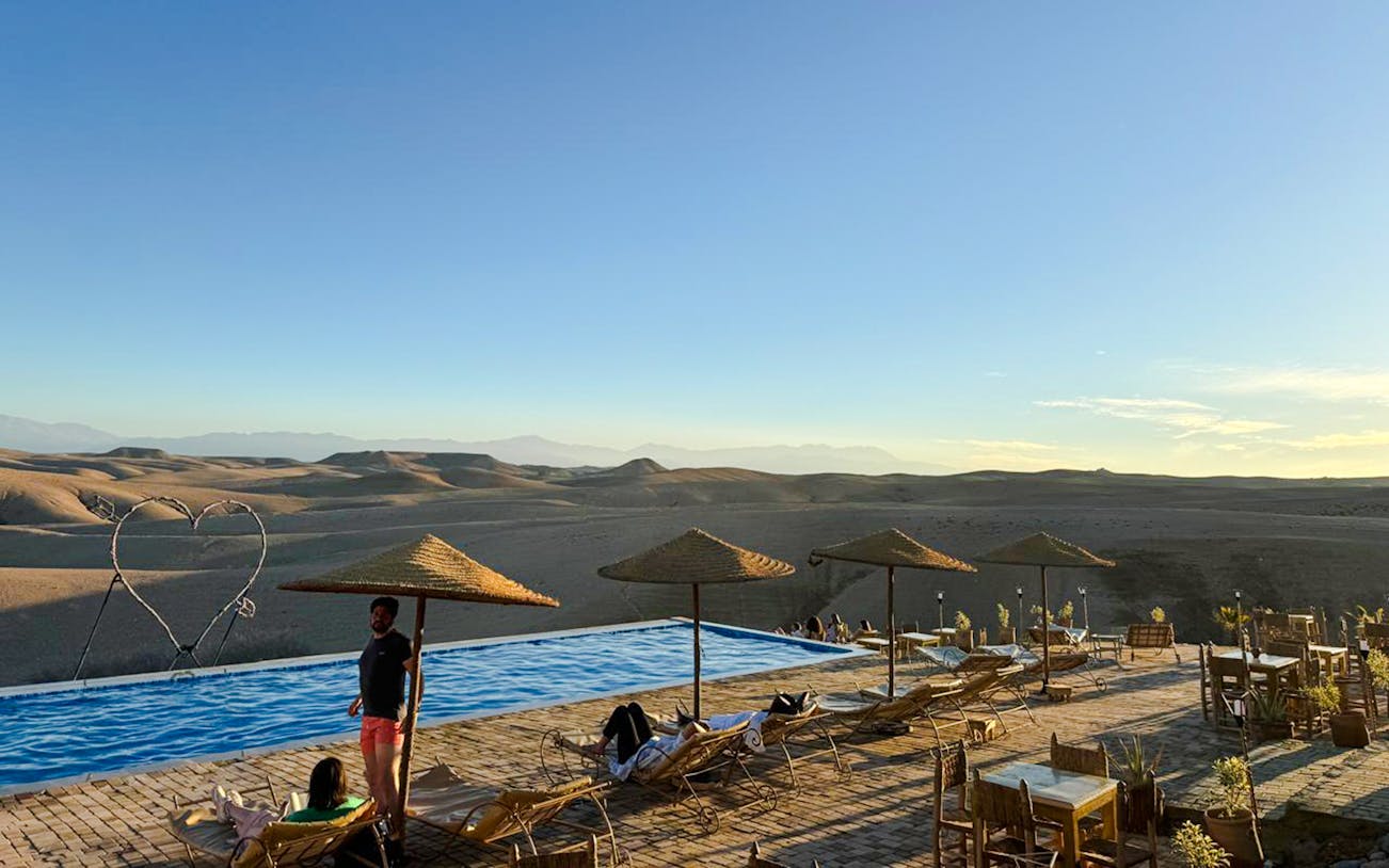 Infinity pool overlooking Agafay desert with lounge chairs and parasols in Marrakesh.