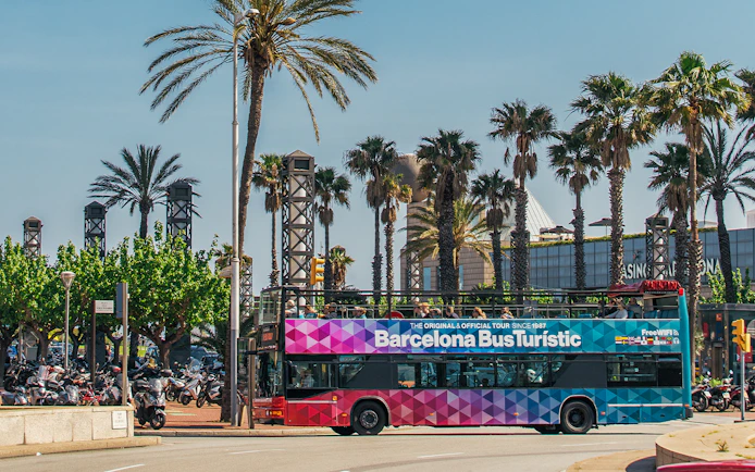Barcelona Bus Turistic passing palm trees on a sunny day.