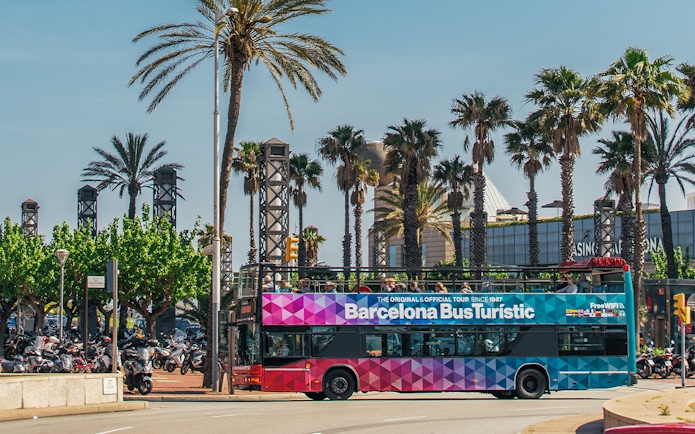 Barcelona Bus Turistic passing palm trees on a sunny day.