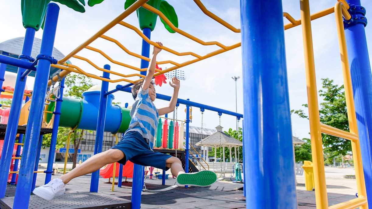 Boy swinging on monkey bars at outdoor playground.