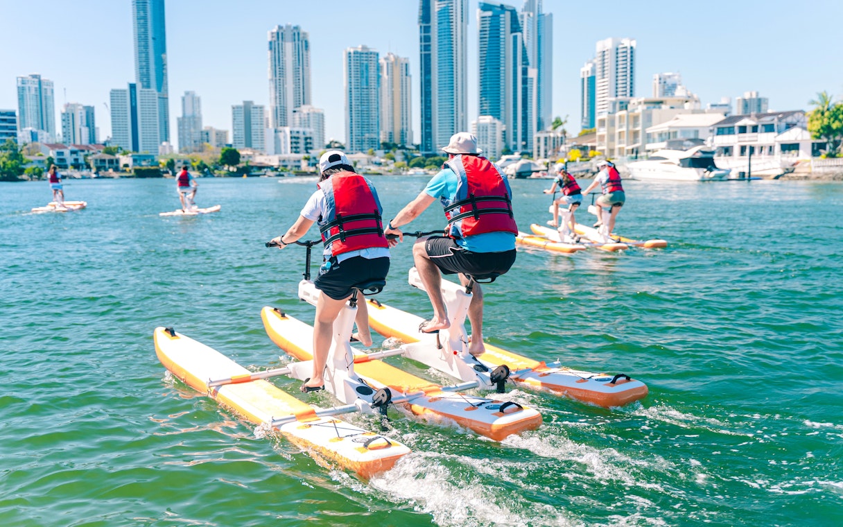 Tourists riding waterbikes on the water with Gold Coast skyline in the background.