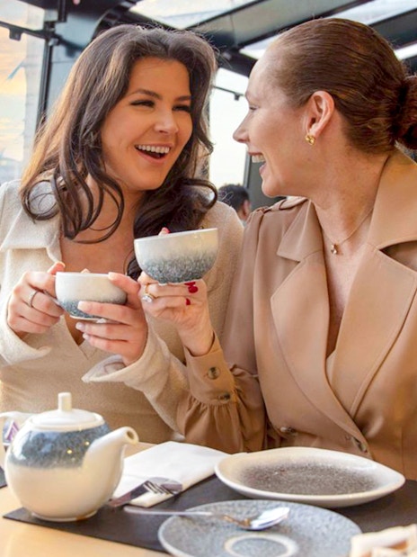 Guests enjoying tea and scones on Thames River Cruise with city view.