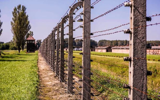Barbed wire fence at Auschwitz-Birkenau concentration camp, Poland, with guard tower in background.