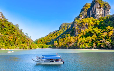 Boat on water with lush hills in Kilim Geoforest Park, Langkawi, Malaysia.