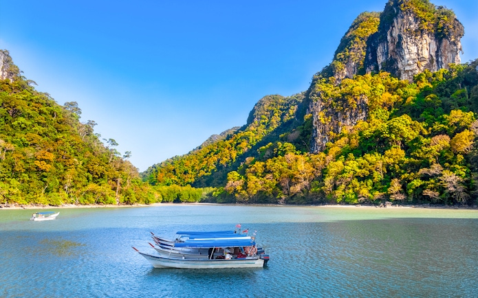 Boat on water with lush hills in Kilim Geoforest Park, Langkawi, Malaysia.