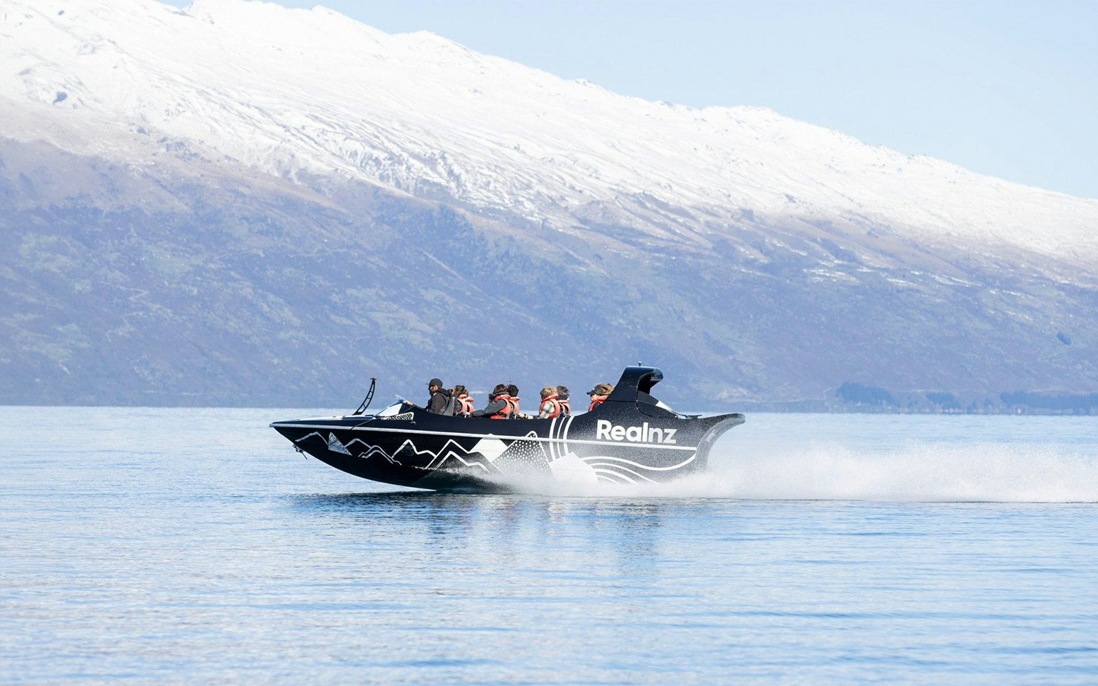 Jet boat speeding on Kawarau River with snow-capped mountains in the background.