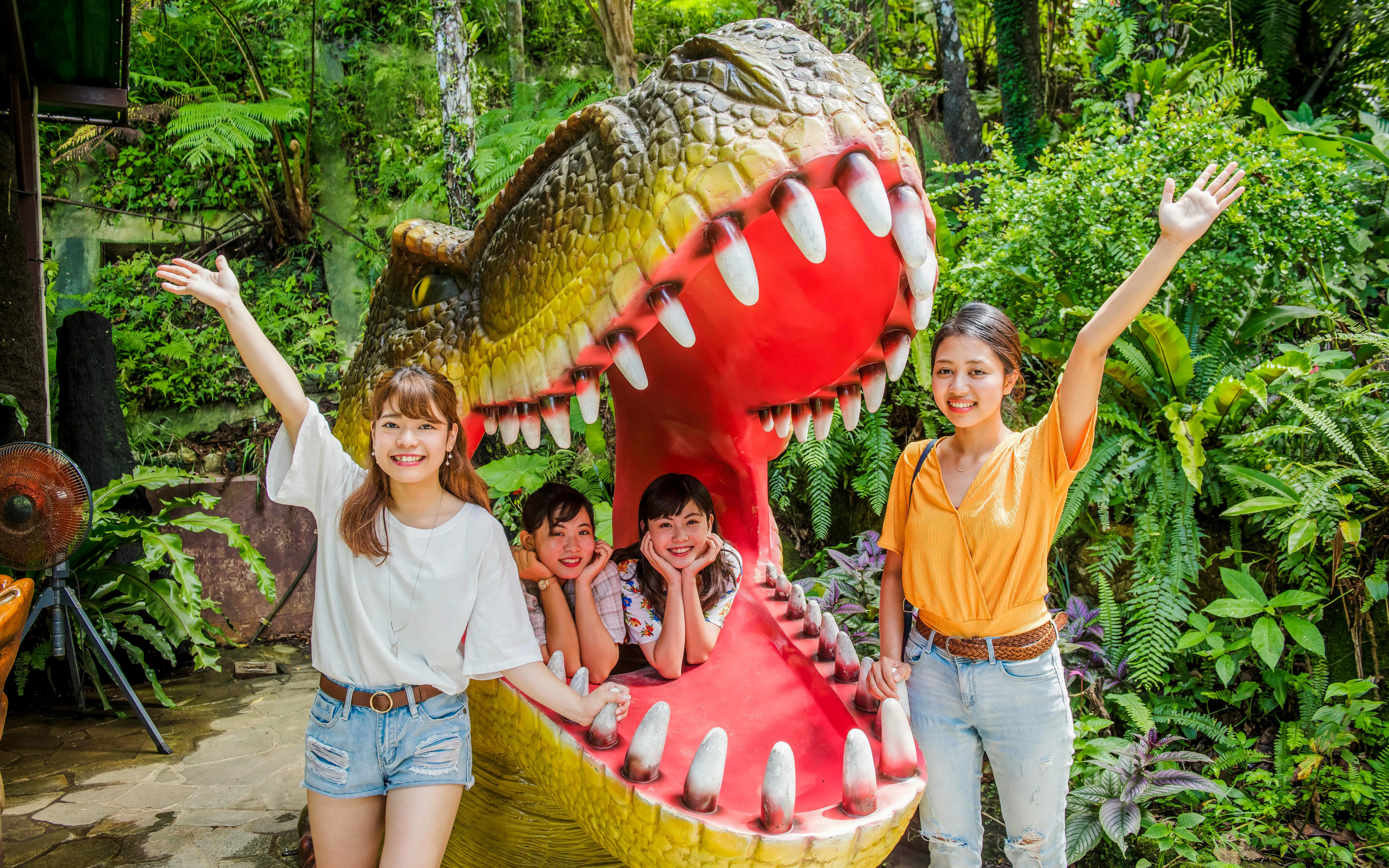 Visitors posing with dinosaur sculpture at Okashigoten Nago Dino Park Yanbaru Subtropical Forest.