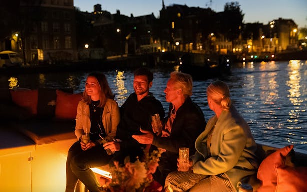 Evening canal cruise with people enjoying drinks in Amsterdam's Red-Light District.