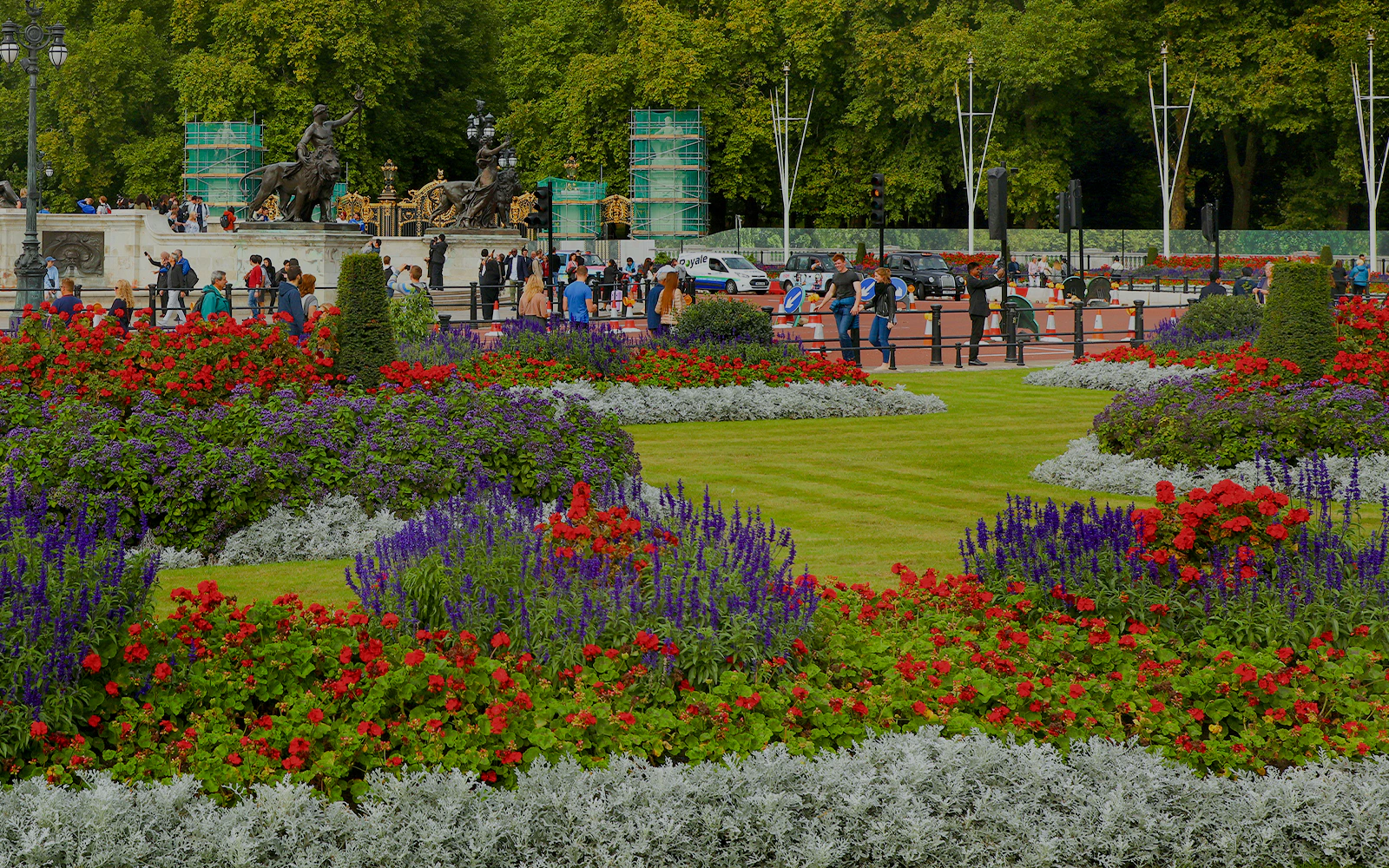 Buckingham Palace gardens with colorful flowers and tourists in London, England.