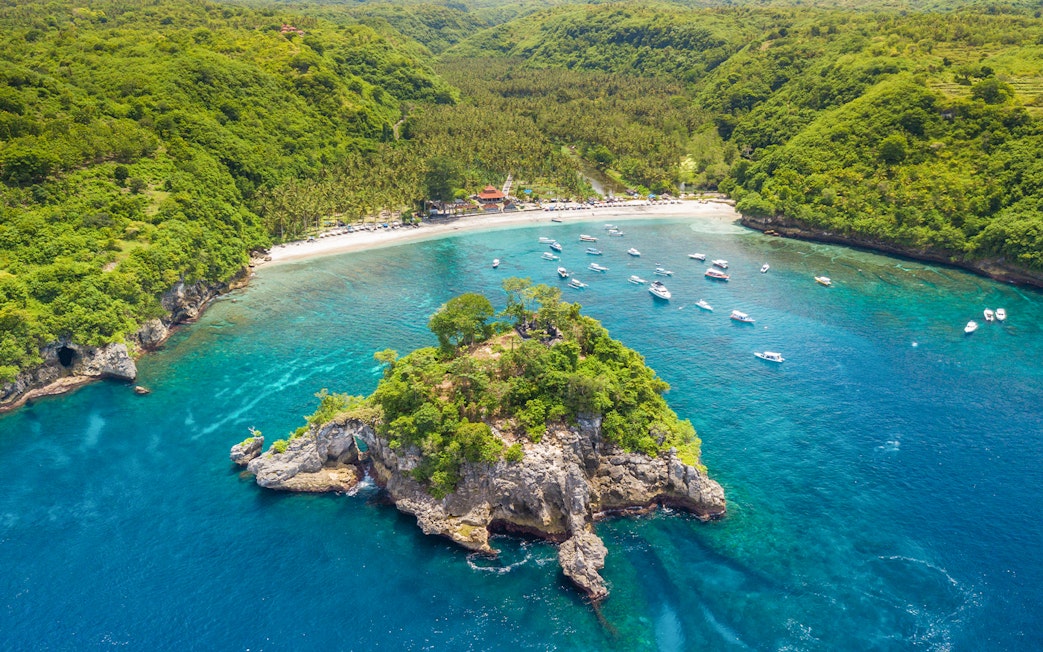 Tourists enjoying the coastline and boats at West Nusa Penida Island, Indonesia.