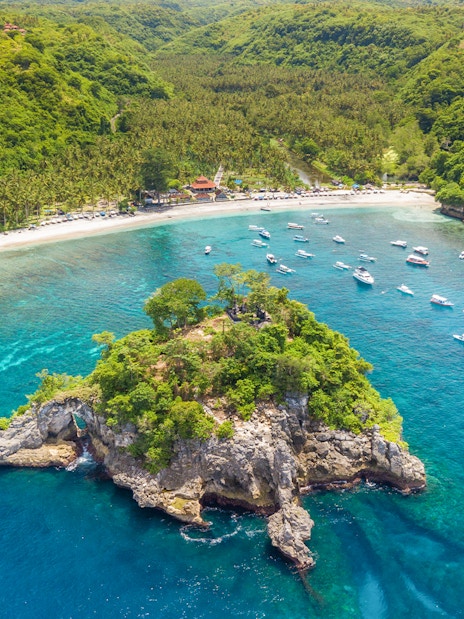 Tourists enjoying the coastline and boats at West Nusa Penida Island, Indonesia.